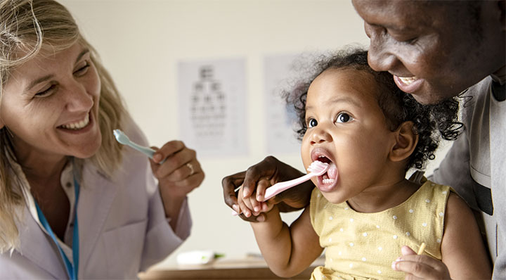 Toddler with learning how to brush her teeth with dad and dental professional