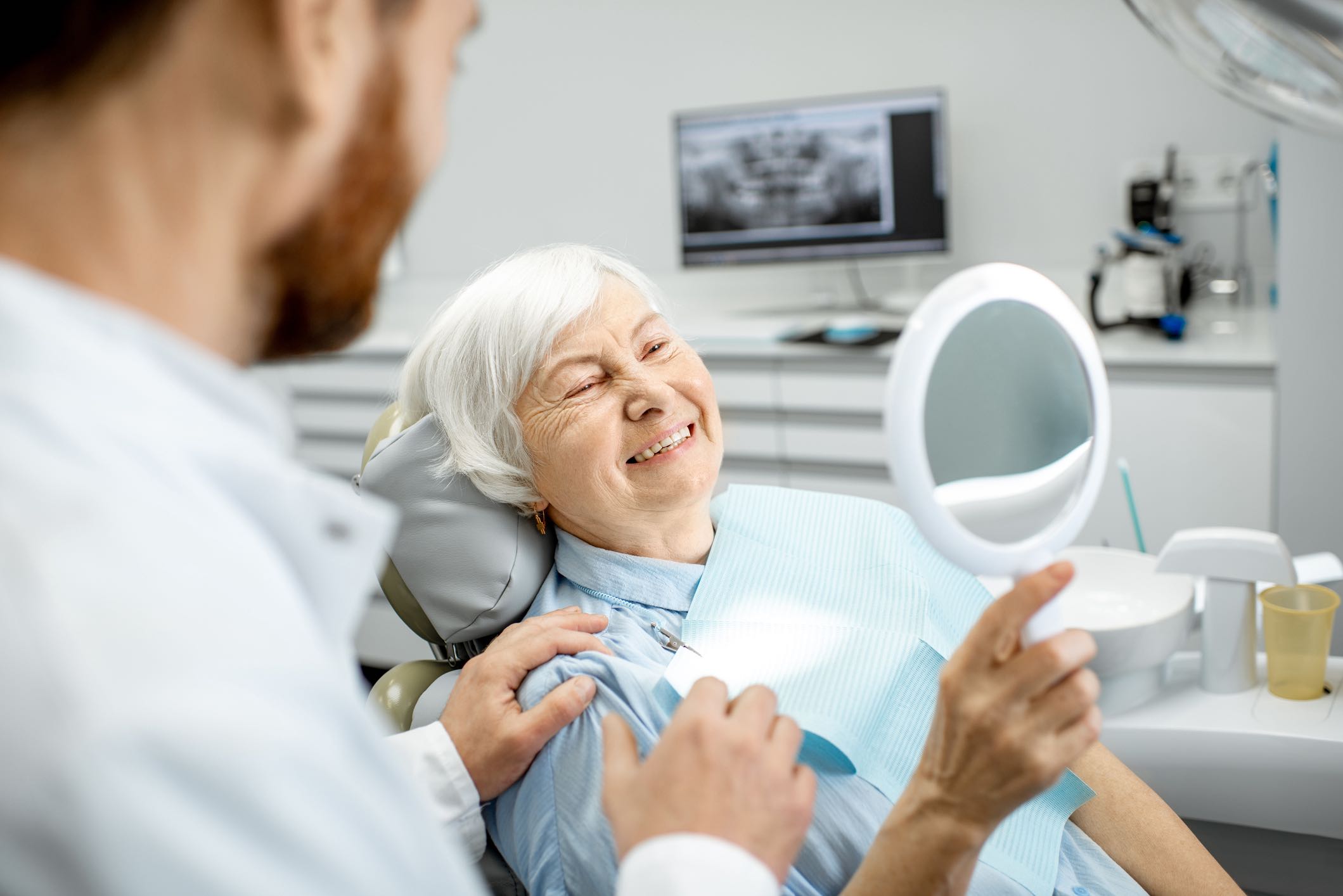 older woman looking at her smile in a handheld mirror at dentist office